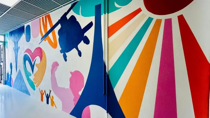 Vue d'ensemble d'un couloir intérieur avec fresque collective colorée et rayons multicolores