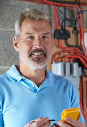 Électricien en polo bleu posant devant un tableau électrique avec un appareil